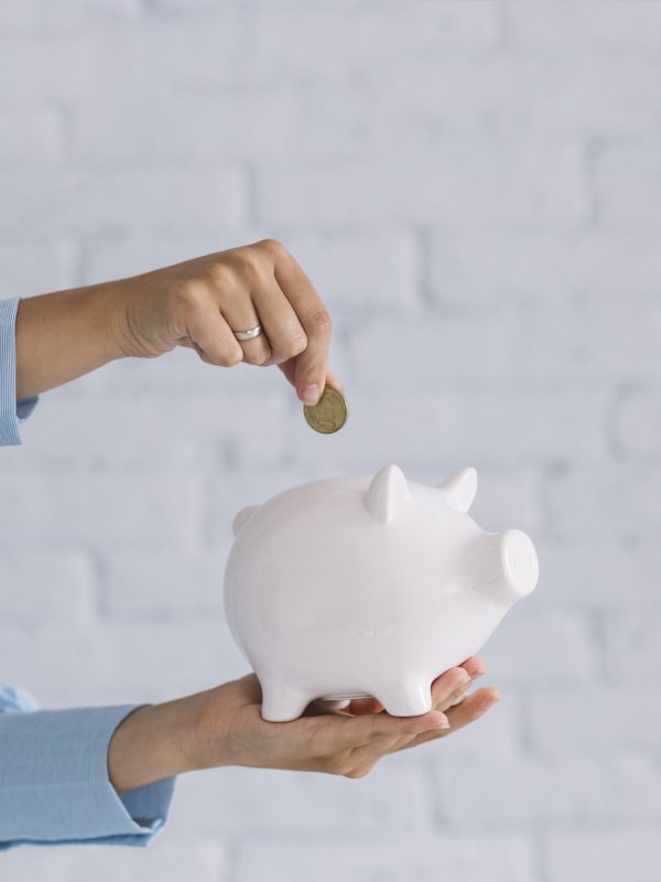 close-up-person-s-hand-inserting-coin-white-piggybank