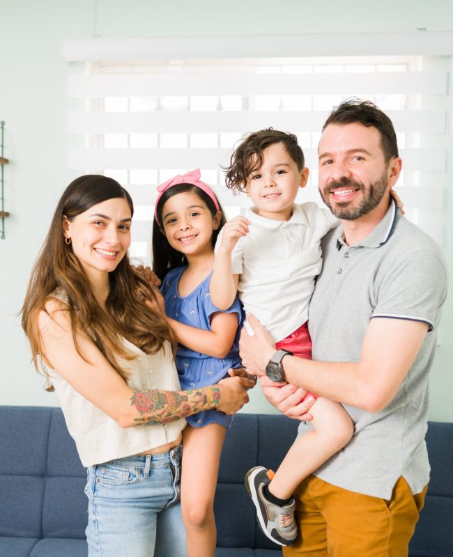 Portrait of a beautiful family of four with adorable little children smiling and making eye contact while spending a relaxing day together at home